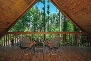 An attic-style room with a wooden deck, two wicker chairs, and a small table.