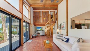 A spacious living area with a white sofa, wooden staircase, and large windows overlooking a deck.