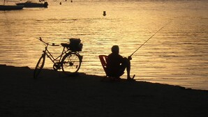 On aperçoit la silhouette d’une personne pêchant au bord de l’eau, avec un vélo garé à proximité.