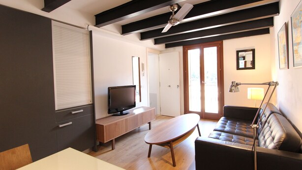 Ein modernes Wohnzimmer mit Flachbildfernseher, Couchtisch aus Holz, Ledersofa und Deckenventilator.