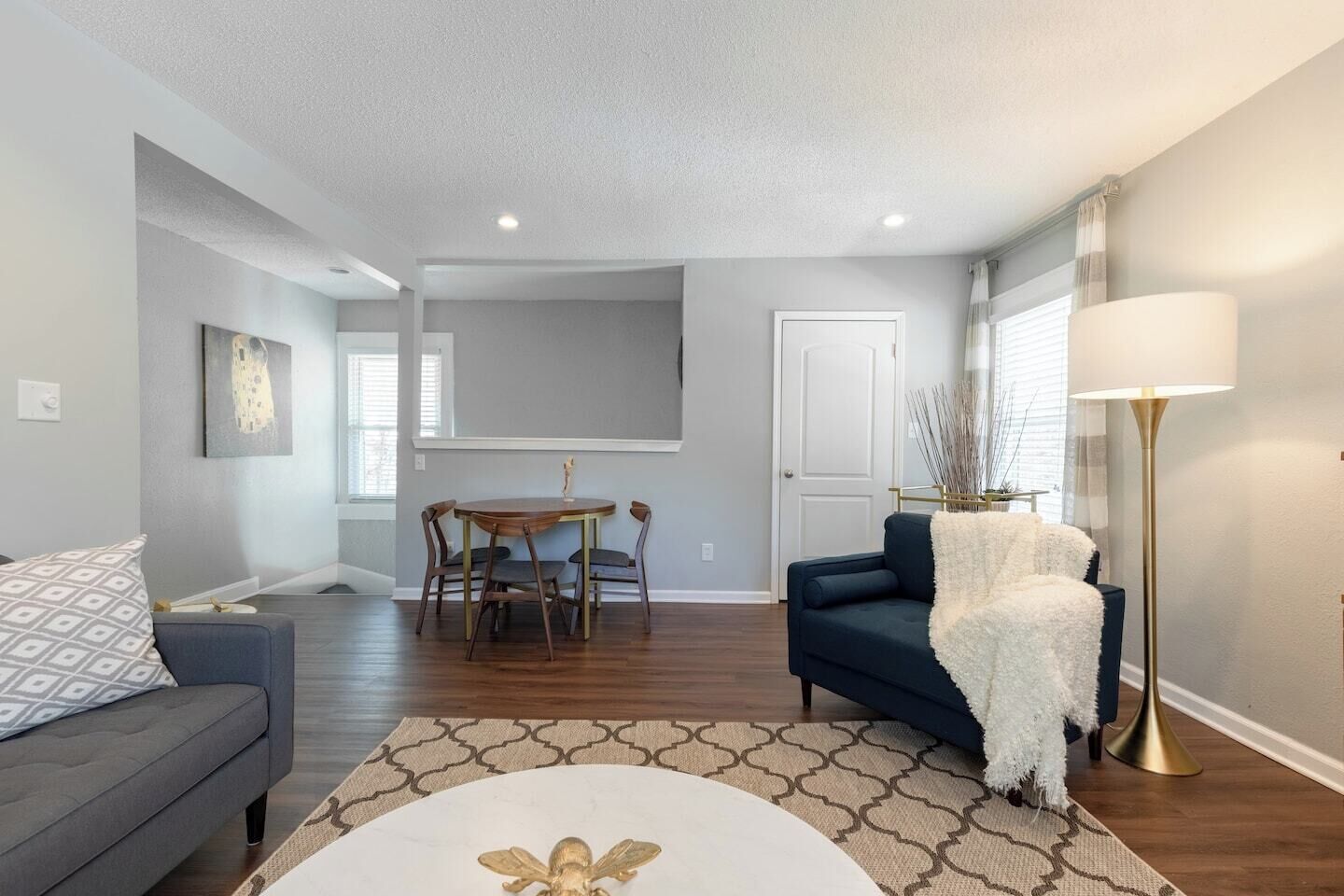 A modern living room with a dark blue sofa, a round dining table with chairs, a white coffee table, and a floor lamp.