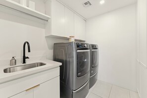 A compact kitchen with a stainless steel sink, a black faucet, and two front-loading washing machines.