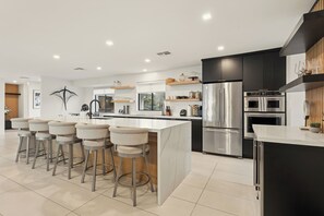 A modern kitchen with a central island, bar stools, stainless steel appliances, and wooden accents.