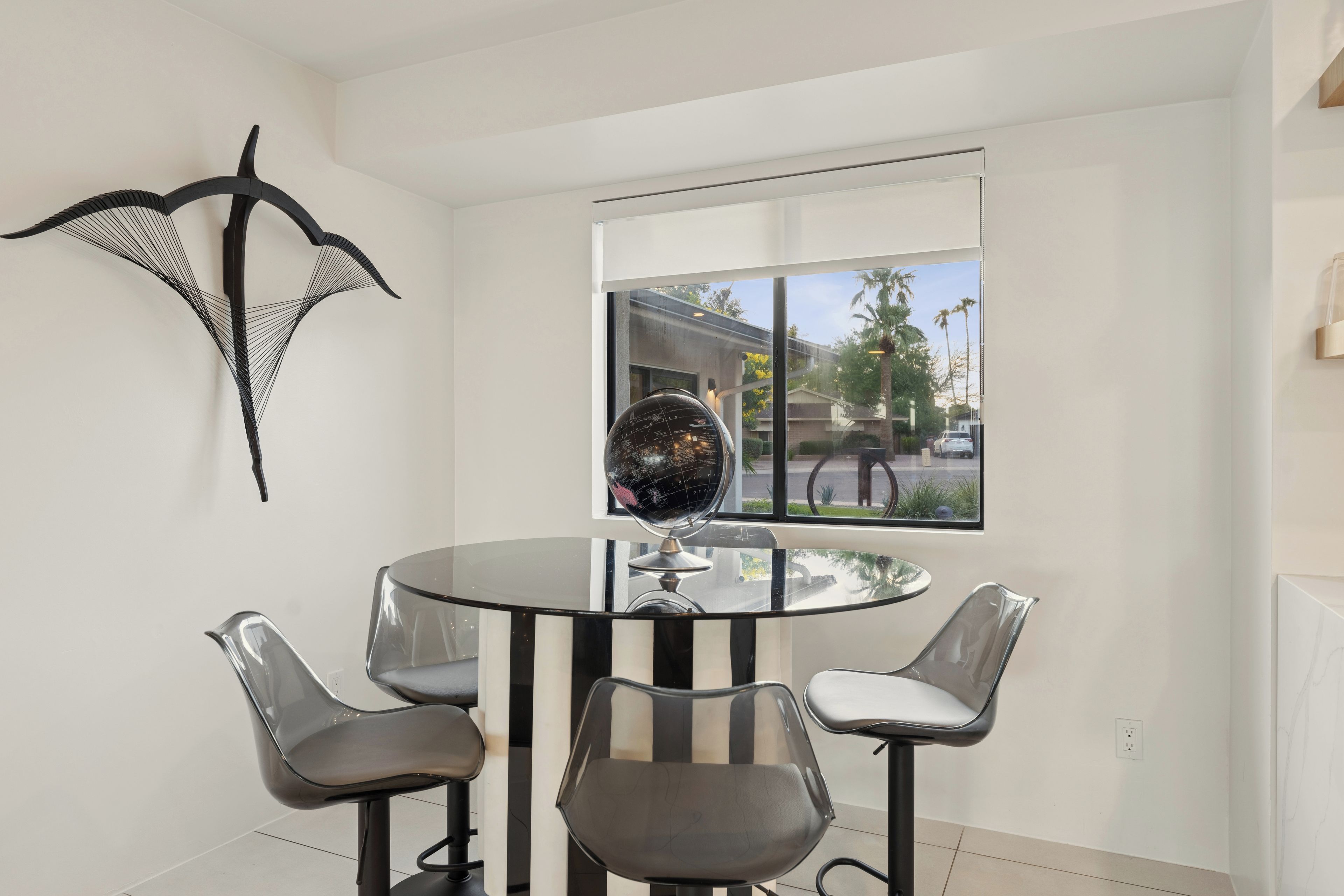 Un interior moderno con una mesa redonda de cristal, cuatro sillas, un globo terráqueo y una obra de arte en la pared.