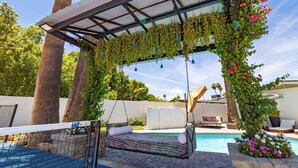 Een zwembadgedeelte met een hangstoel, een overdekte zithoek en een pergola met hangende planten.