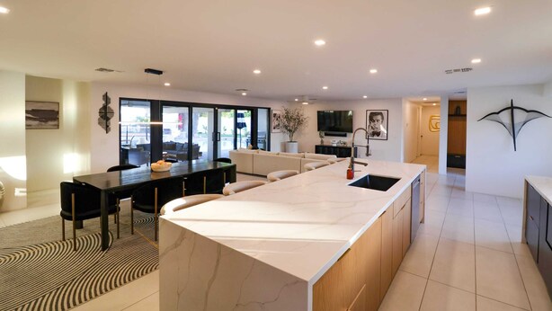 Een moderne keuken met een marmeren eiland, zwarte stoelen en een eethoek met een vloerkleed met een patroon.