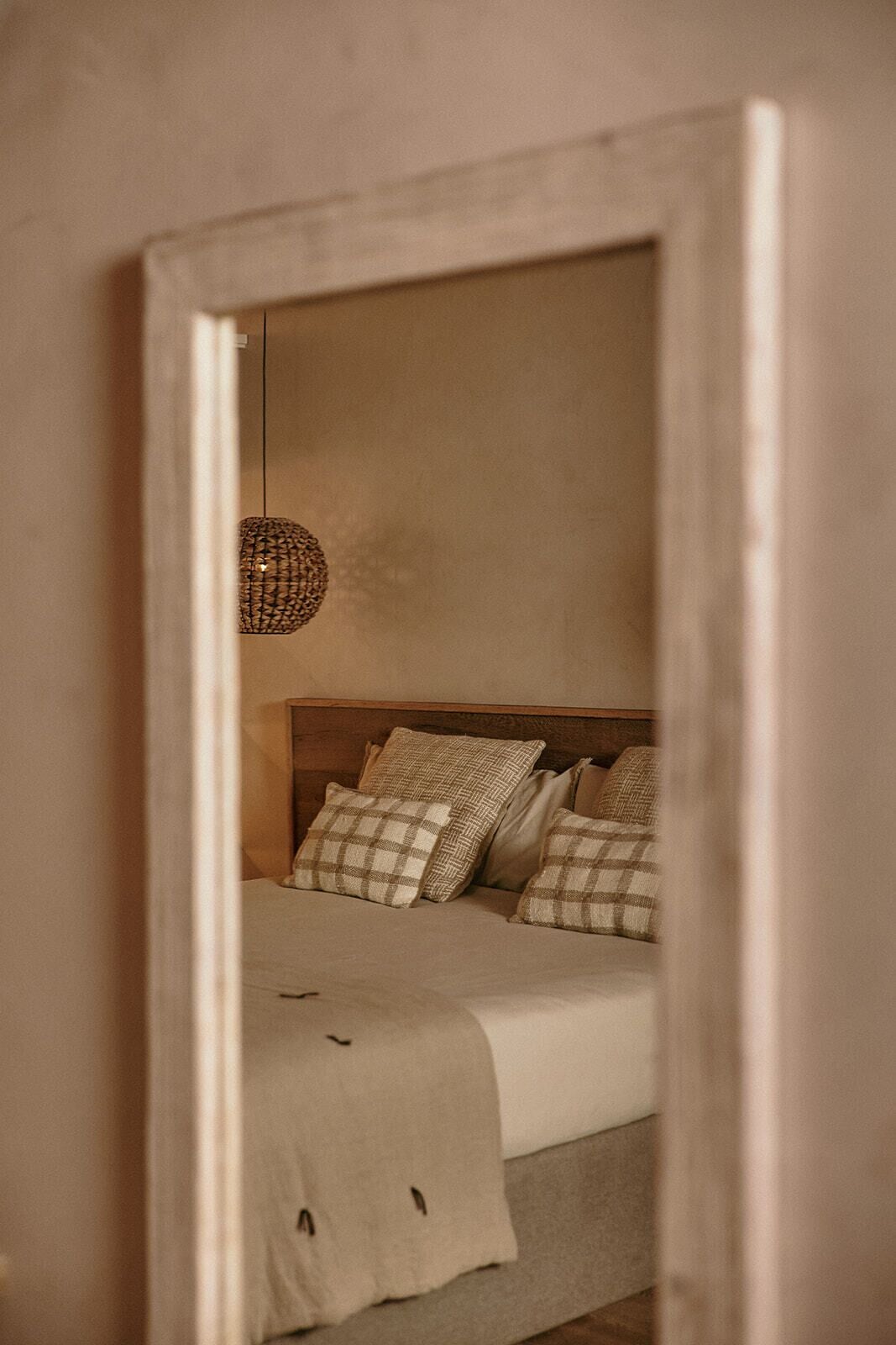 A bedroom with a bed, pillows, a hanging light fixture, and a mirror reflecting the room.