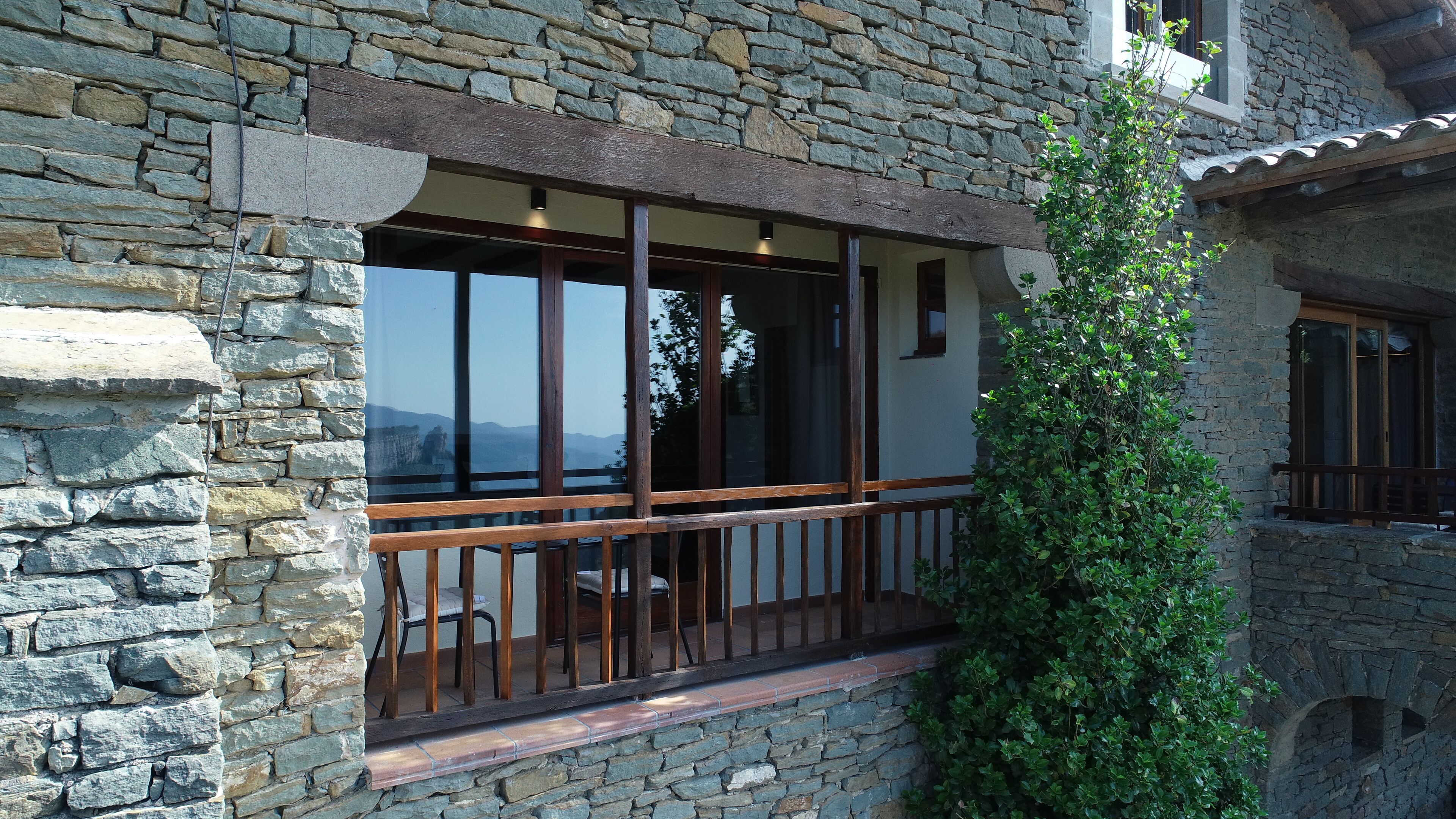 A stone building with a balcony, large windows, and a view of the landscape.