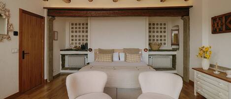 A bedroom with a double bed, two armchairs, a small round table, a dresser, and a mirror.