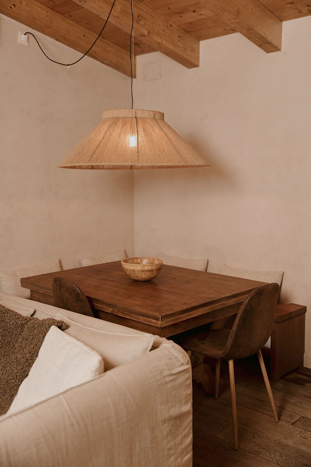 A dining area with a wooden table, chairs, a hanging lamp, and a bowl on the table.