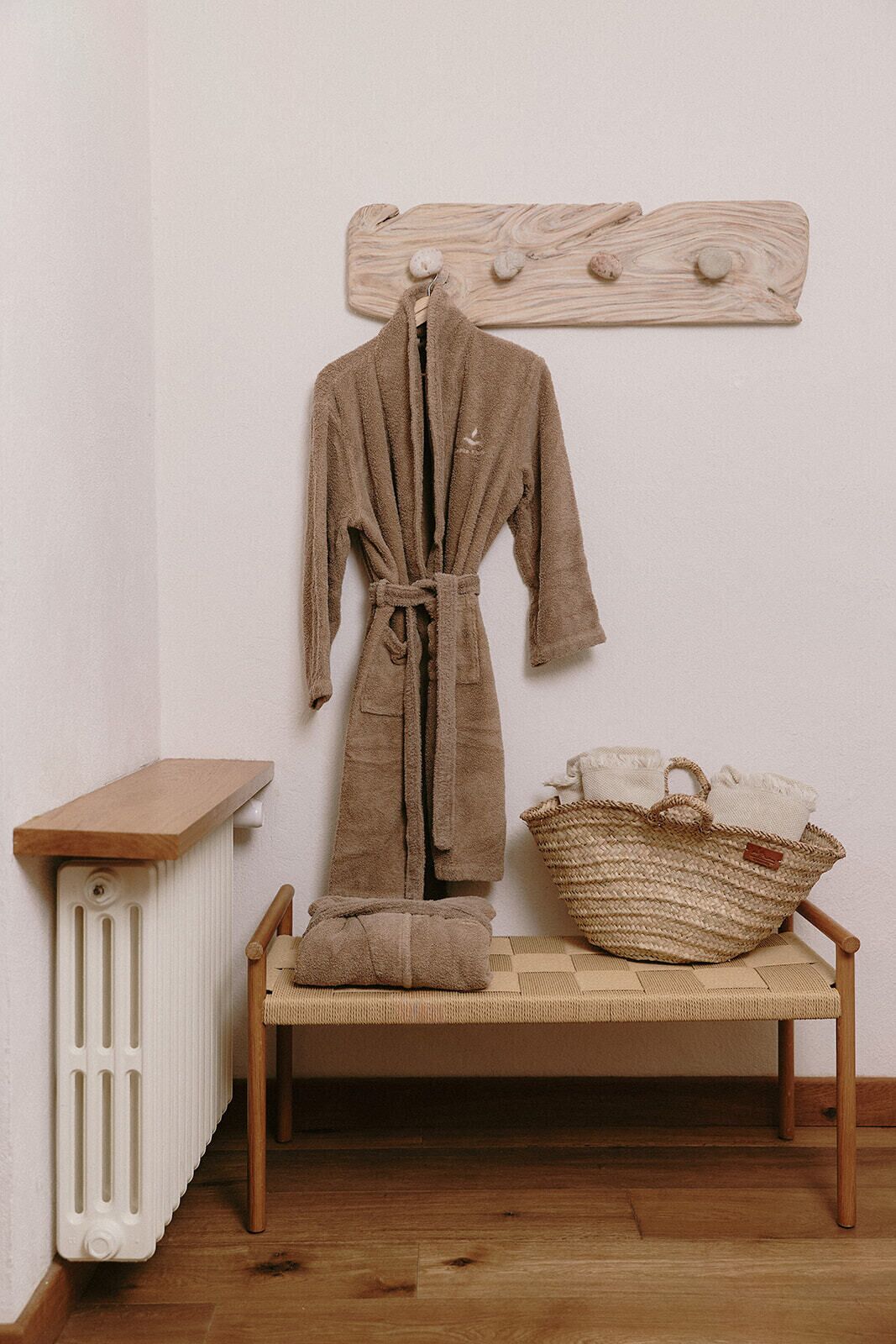 Un banc de fusta amb una cistella teixida, una bata marró i un radiador.