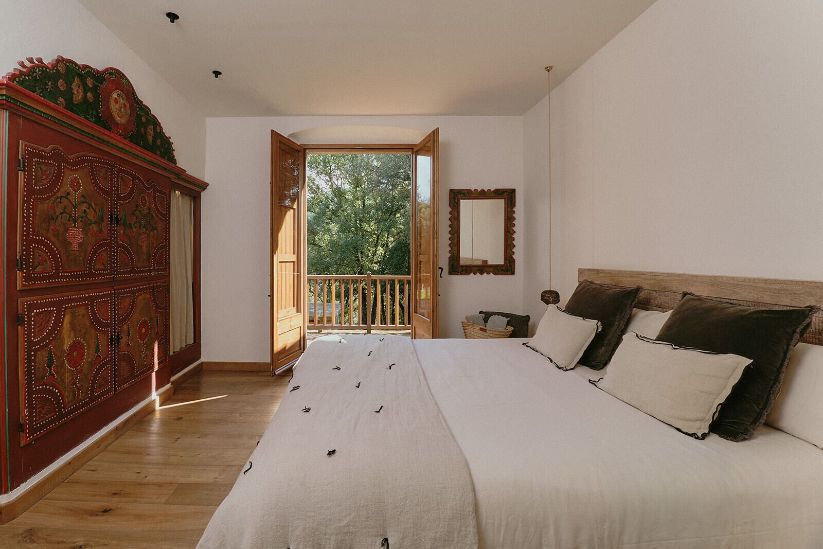Quarto com cama grande, guarda-roupa de madeira, varanda e vista para árvores.