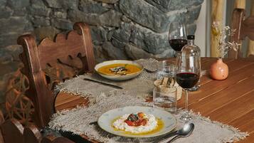 A rustic dining table with a stone wall backdrop, wooden chairs, a placemat, and a bottle of red wine.