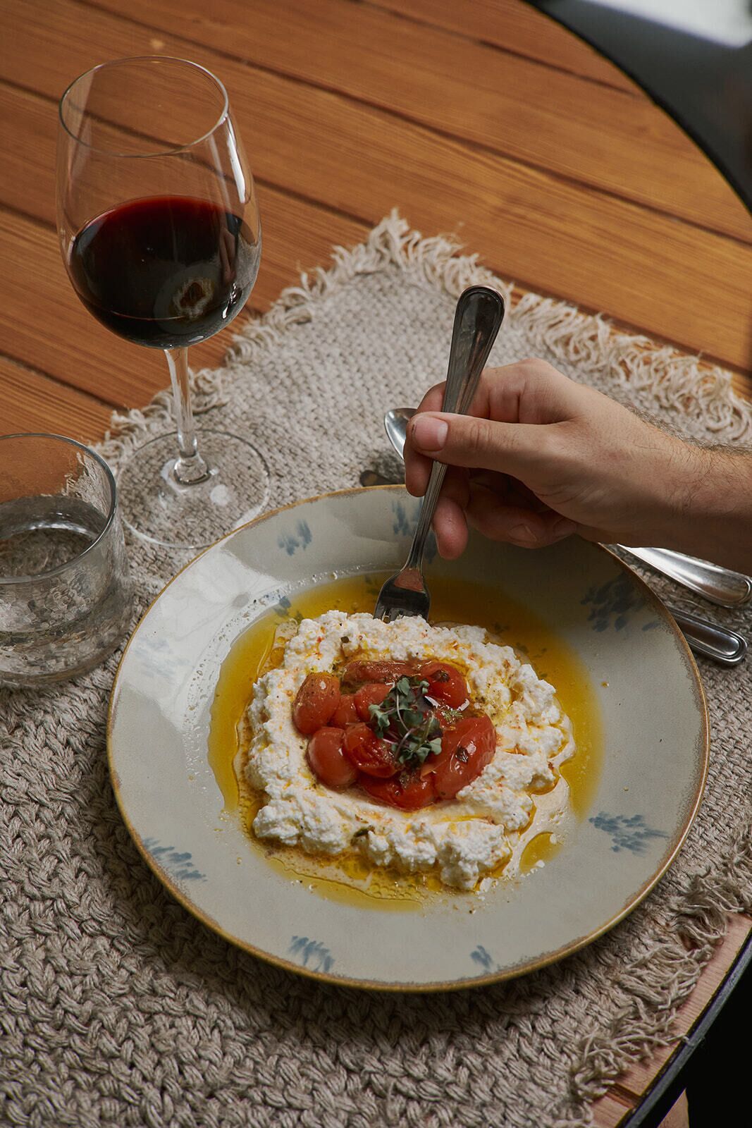 A plate of food with a spoon and a glass of red wine on a table.