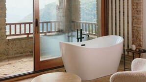 A bathroom with a freestanding bathtub, a wooden-framed ceiling, and a view of a balcony with a railing. - Hotel Santa Llucia Rupit (Rupit I Pruit)