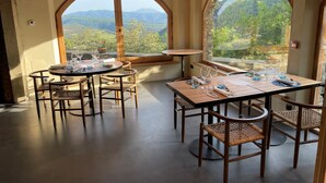 A dining area with round tables and wicker chairs, large arched windows offering a view of a mountainous landscape. - Hotel Santa Llucia Rupit (Rupit I Pruit)