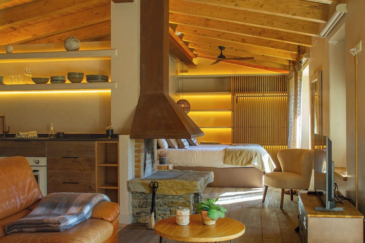 Una habitación acogedora con cama, techo de madera, chimenea de piedra, zona de comedor y televisor.