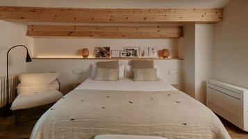 Un dormitorio con cama, almohadas, una silla, estante con fotografías y un radiador.
