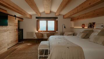 Een slaapkamer met een groot bed, houten balken, een raam, een bureau en een stoel.