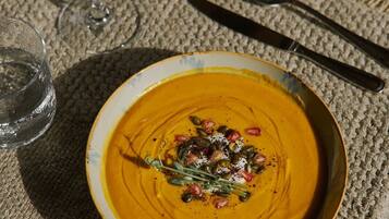 Une table avec un bol de soupe garni de graines et d’herbes, un verre de vin rouge et des couverts.