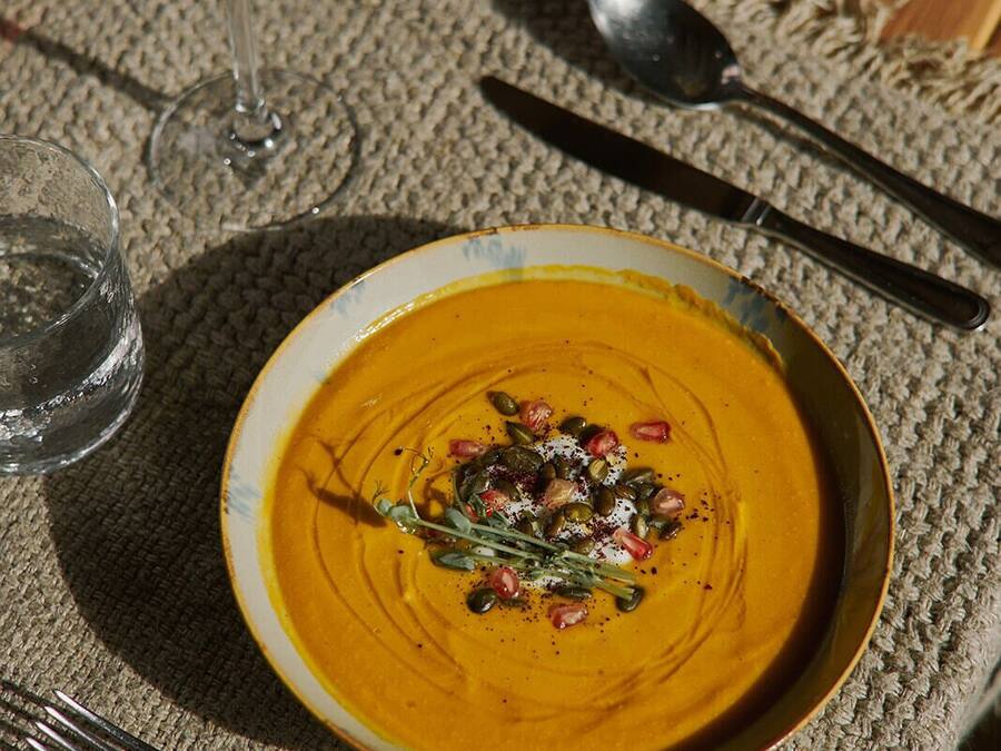 Une table avec un bol de soupe garni de graines et d’herbes, un verre de vin rouge et des couverts.