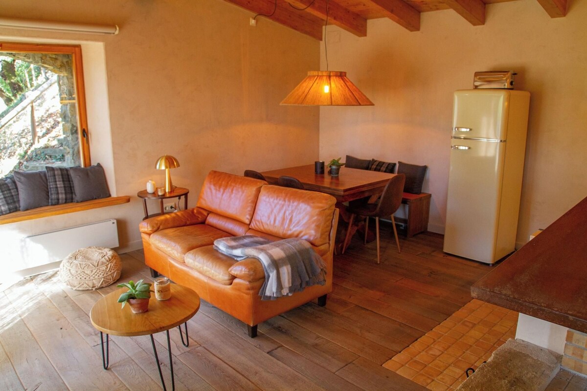 A cozy living room with a leather sofa, a dining table, a small round table with a lamp, and a refrigerator.