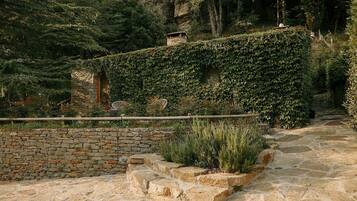 Ein gepflasterter Weg führt durch einen Garten mit einer Steinmauer und einer Holzbank.