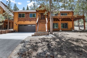 A two-story wooden cabin with a front staircase, a garage, and a covered porch.
