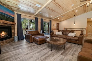 A cozy living room with a fireplace, leather sofas, and a large window overlooking a deck.