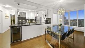 Una cocina moderna con una mesa de comedor de vidrio, sillas negras y vistas a la ciudad a través de grandes ventanales.