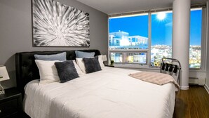 Un dormitorio moderno con una cama grande, vistas a la ciudad y un cuadro abstracto único en la pared.