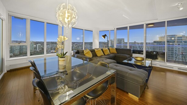 Una sala de estar moderna con una mesa de comedor de vidrio, sofá de cuero y amplias ventanas con vistas a la ciudad.