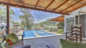 Un espace extérieur abrité, doté d’une piscine, de mobilier en bois et offrant une vue sur le paysage environnant.