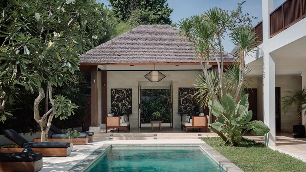 A swimming pool with lounge chairs, a covered seating area, and tropical plants. - Villa Amara Pradi (Seminyak)