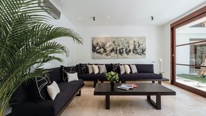 A modern living room with a black sectional sofa, a coffee table, and a large abstract painting on the wall. - Villa Amara Pradi (Seminyak)