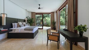 A modern bedroom with a large bed, a desk, and a chair. There is a window with curtains and a view of greenery outside. - Villa Amara Pradi (Seminyak)