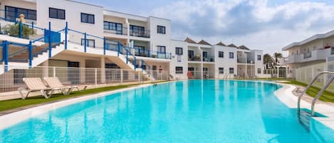 Une piscine avec des chaises longues, un escalier et un immeuble à plusieurs étages doté de balcons.