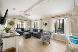 Un salón espacioso con un conjunto de sofás, un sillón estampado y vistas al exterior a través de amplios ventanales.