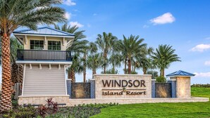 A sign for Windsor Island Resort with a view of the resort's entrance, palm trees, and a building with a blue roof.