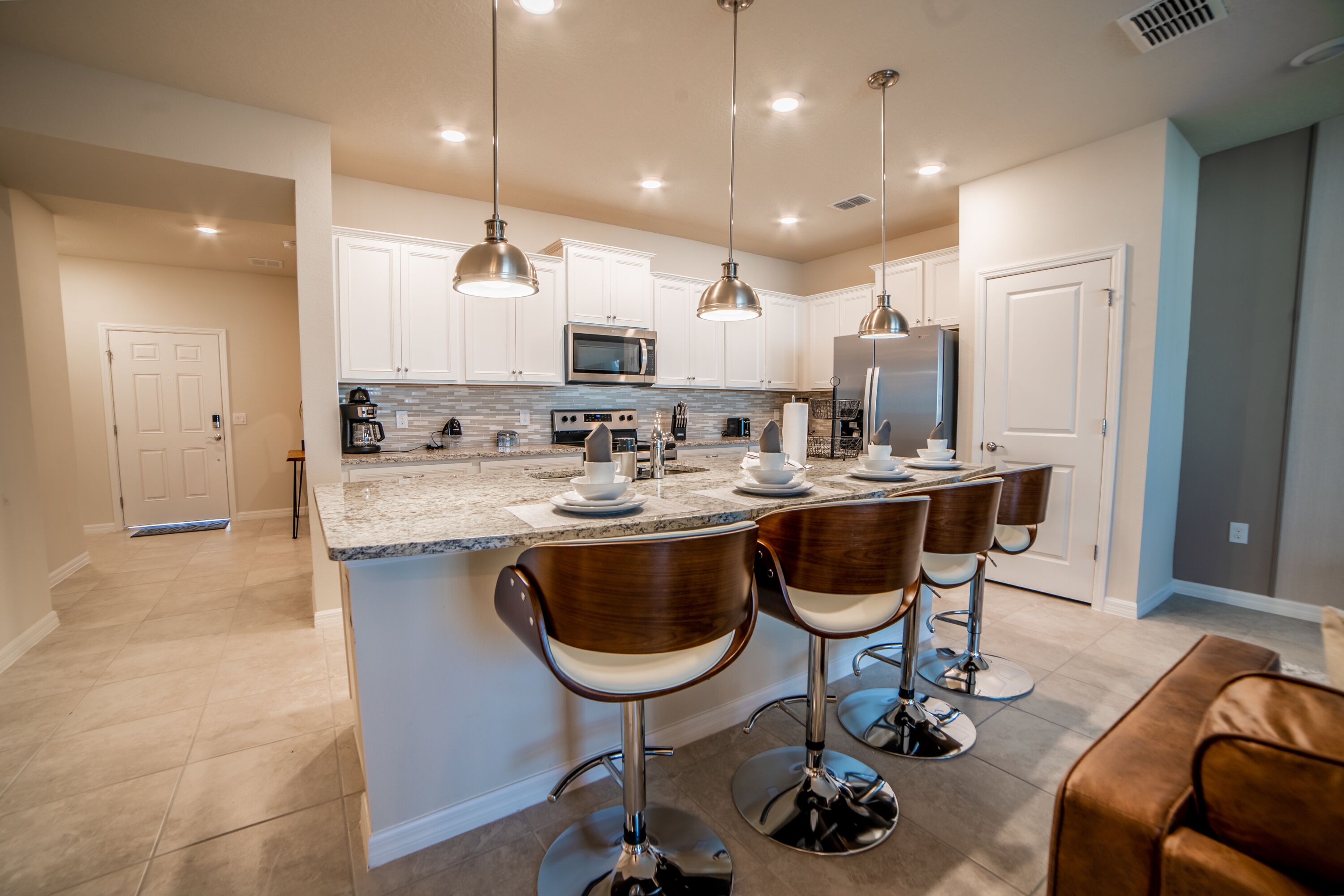 Une cuisine moderne avec des meubles blancs, des appareils en acier inoxydable et un îlot central doté de tabourets de bar.