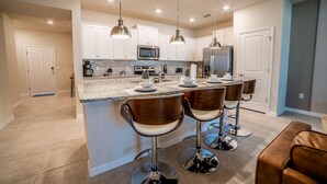 A modern kitchen with white cabinets, stainless steel appliances, and a central island with bar stools.