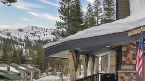 Uma cabana de madeira com varanda, rodeada por montanhas e árvores cobertas de neve.