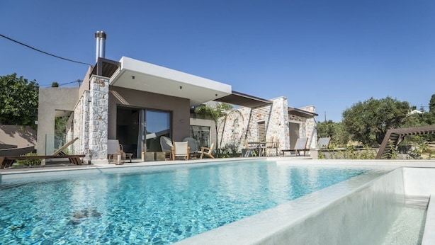 Una casa moderna con piscina, fachada de piedra y zona de estar exterior.