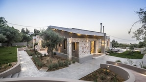 Una casa moderna con fachada de piedra, un jardín cuidado y una vista despejada del paisaje circundante.