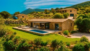 Una villa de piedra con piscina, mobiliario exterior y vistas a las colinas circundantes.