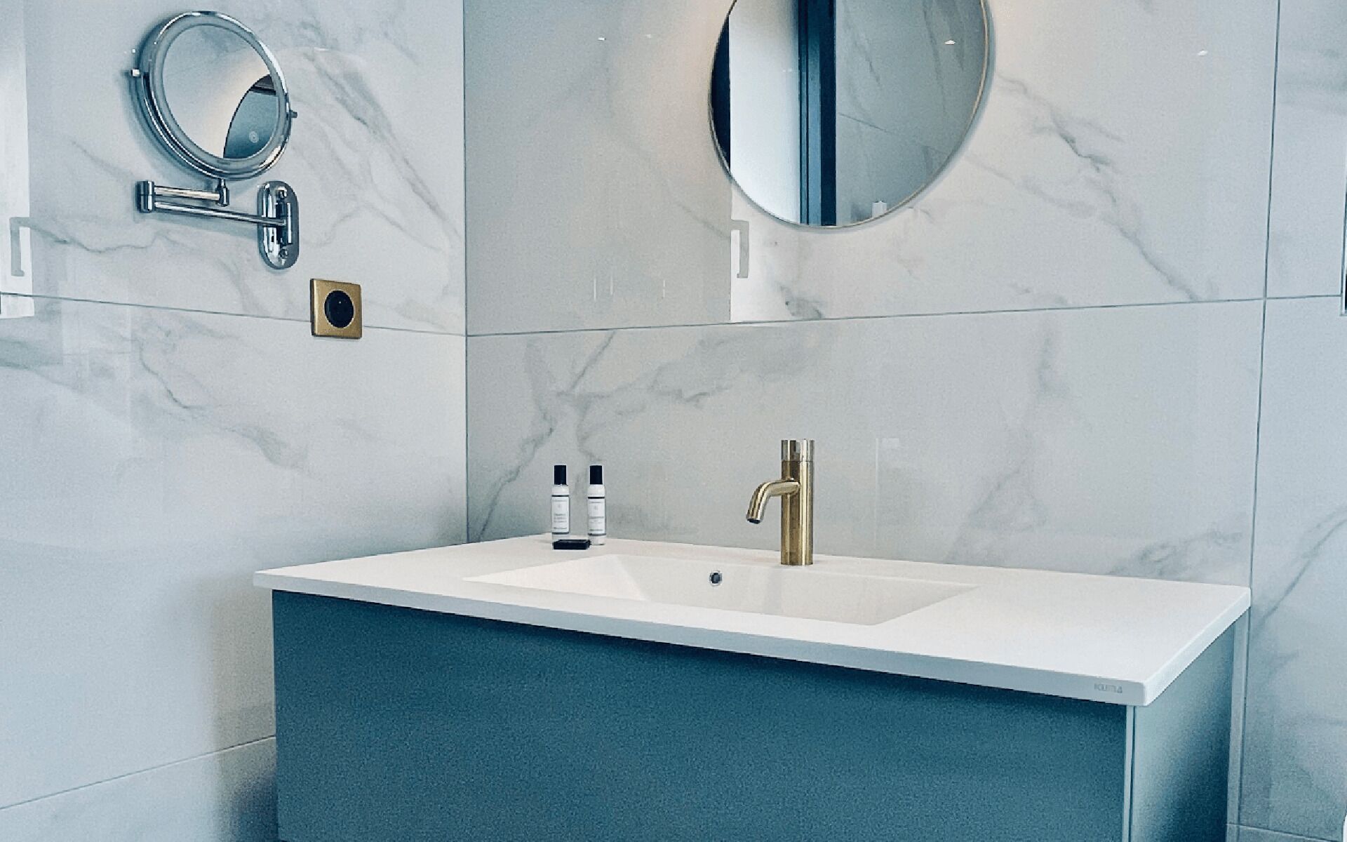 A bathroom with a white sink, a gold faucet, and two round mirrors.