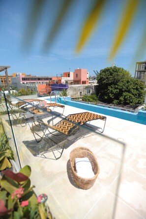 Uma área de piscina no terraço, com espreguiçadeiras e uma pequena mesa, rodeada por edifícios e vegetação.