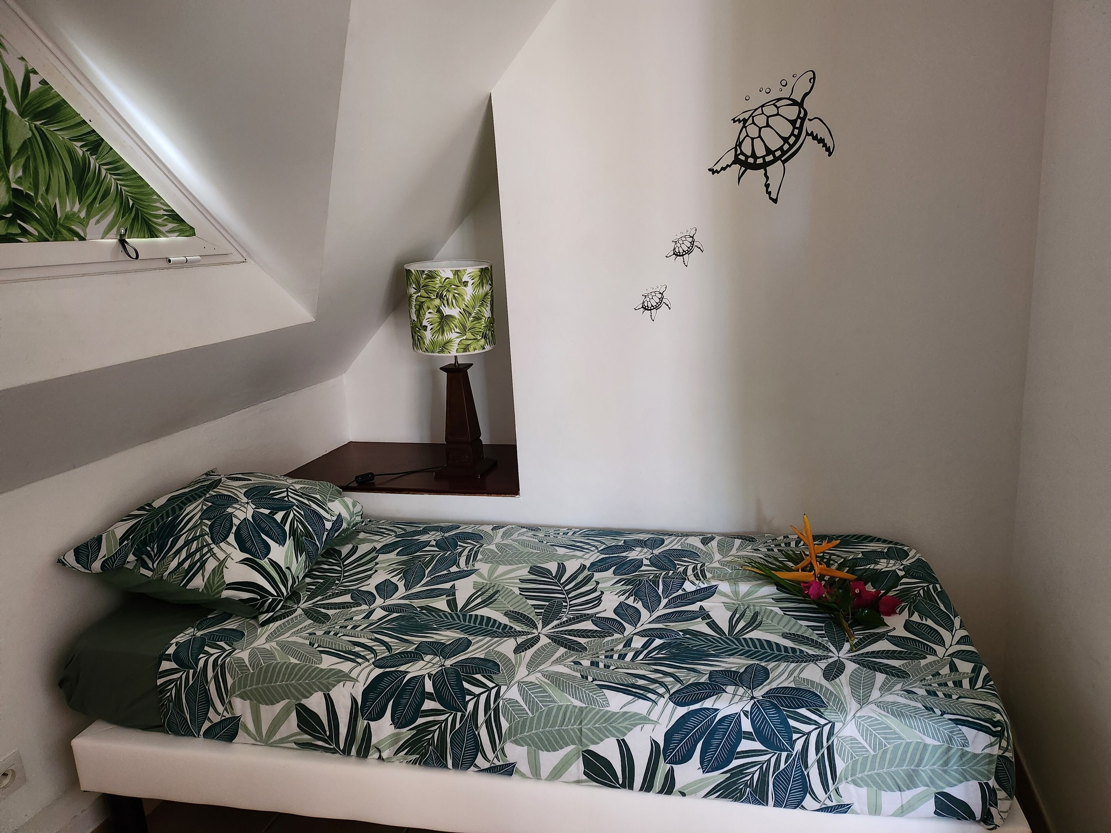 Ein Schlafzimmer mit Bett, Nachttisch, Lampe und Wand mit Schildkrötenmotiv.