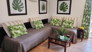 Een woonkamer met een zithoek, een salontafel en wanddecoratie met een tropisch thema.