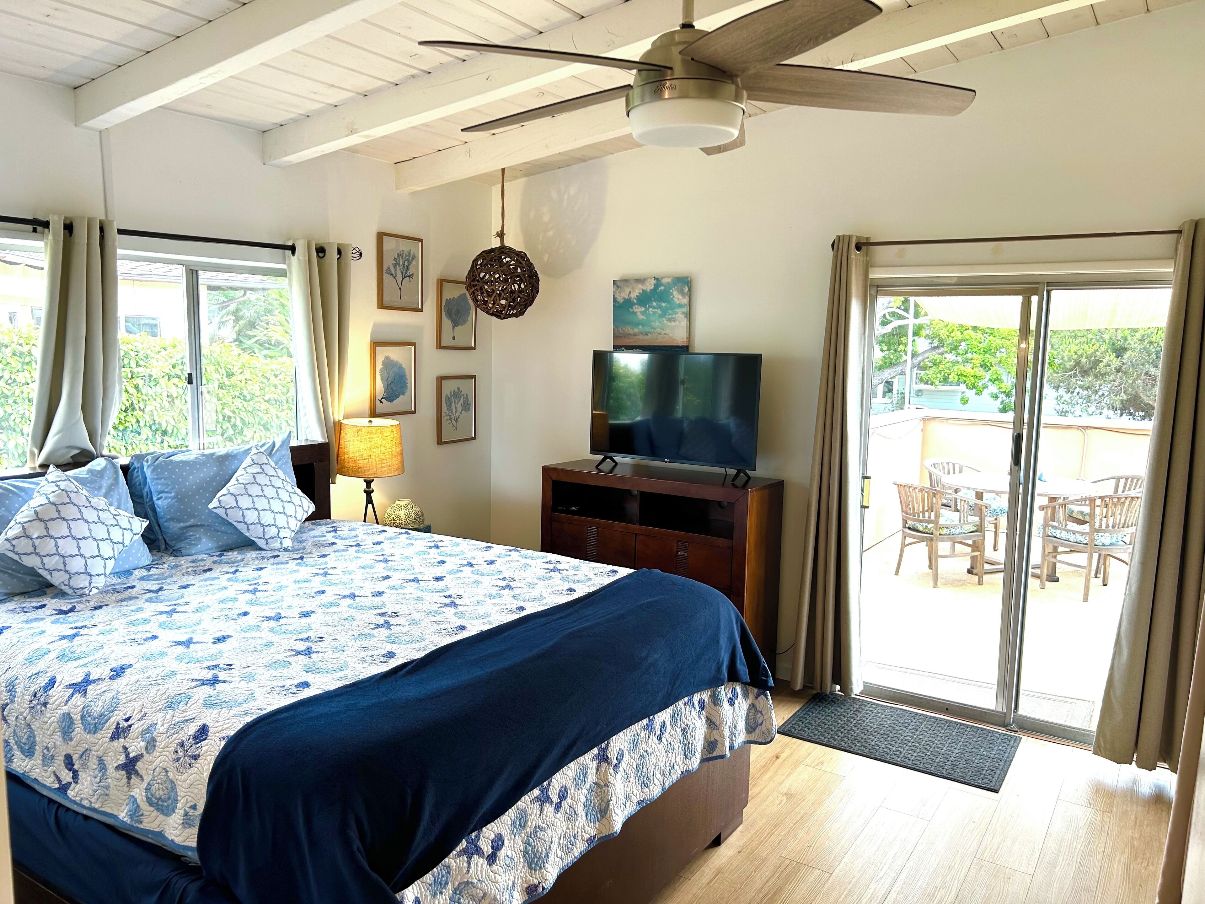 A bedroom with a bed, a TV, a ceiling fan, and a sliding glass door to a patio with outdoor furniture.